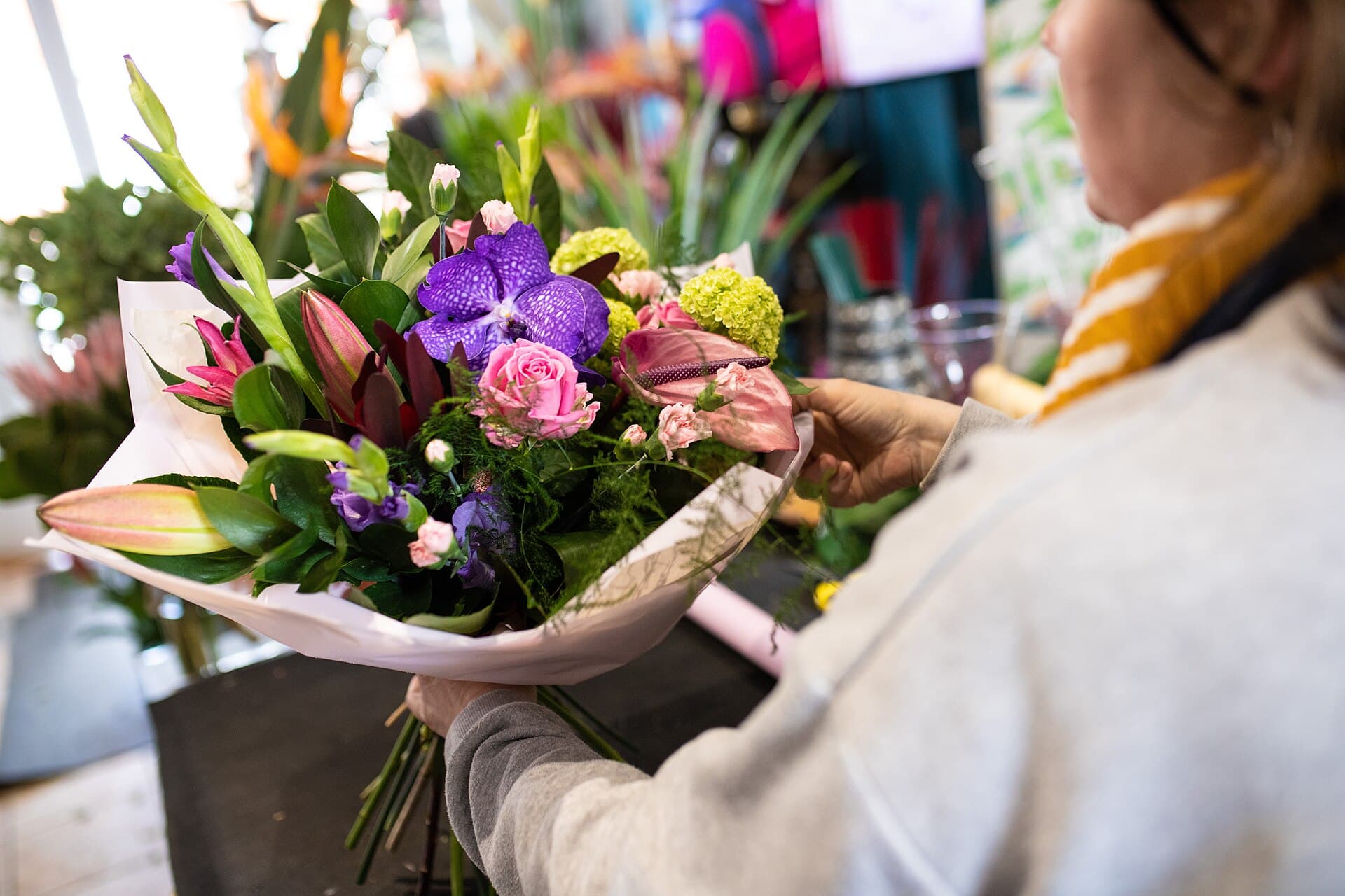 A florist wrapping a bouquet of lilies and orchids at the counter